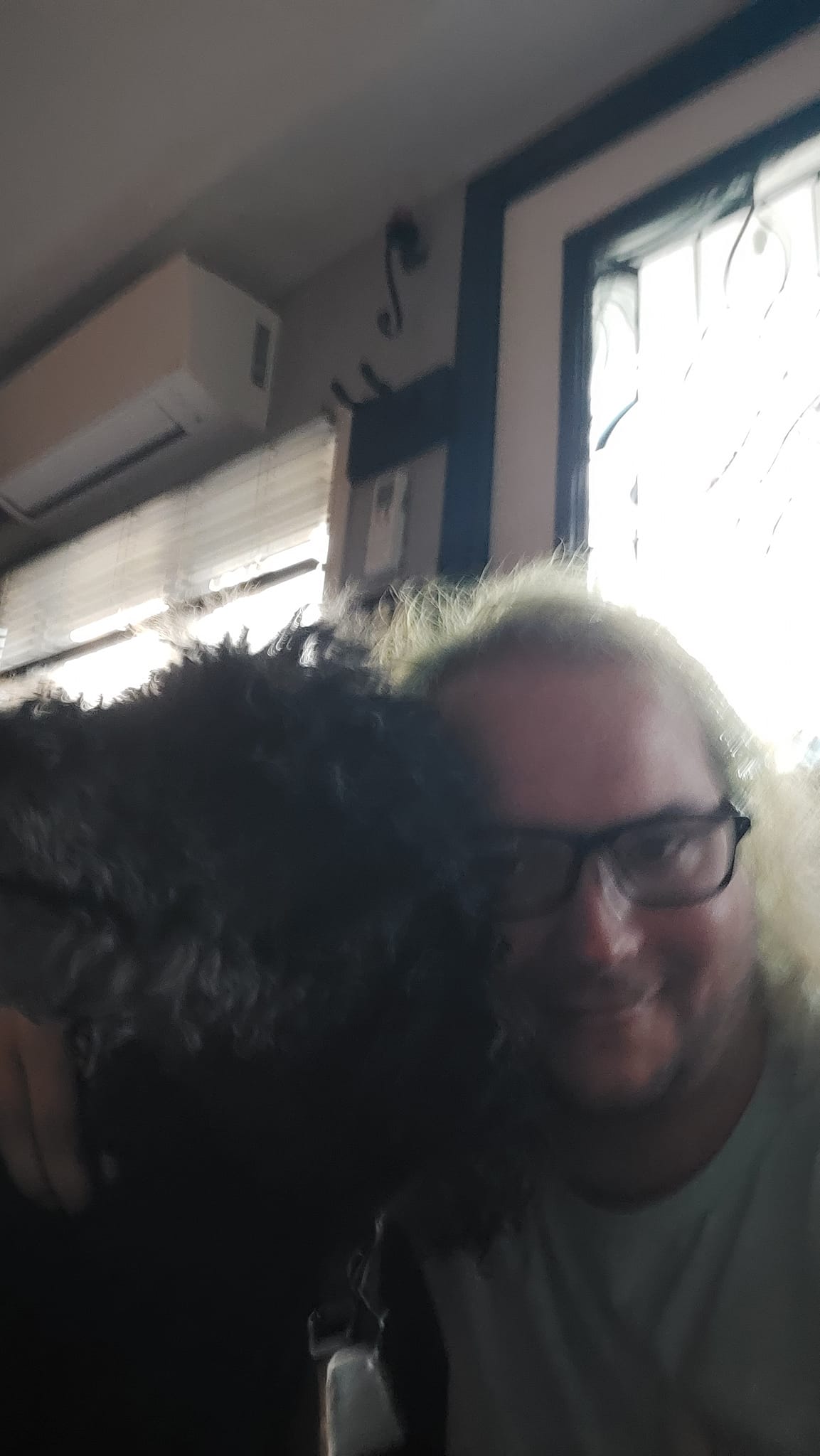 A man with long green hair is hugging a black standard poodle